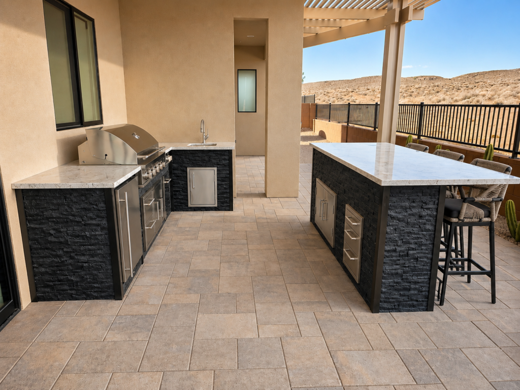 Outdoor kitchen with a built-in stainless steel grill, sink, and marble countertops on dark stone cabinets, set on a tiled patio.
