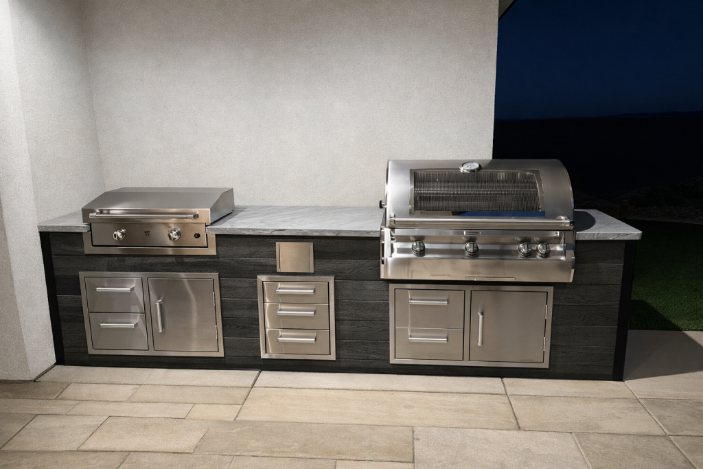 Outdoor stainless-steel grilling station with two built-in grills, multiple drawers, and a marble counter against a beige wall.